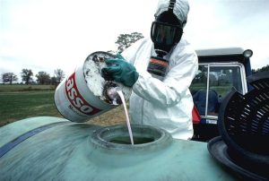 A worker pouring a hazardous pesticide into a container while wearing protective gear