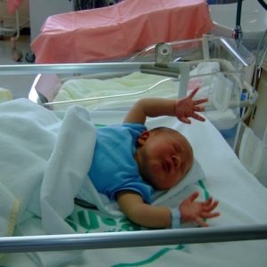An infant in a bassinet has arms stretched out