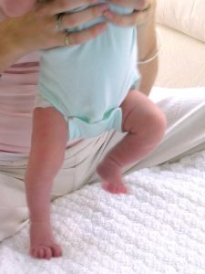An infant's feet touch the ground while the infant is being held upright